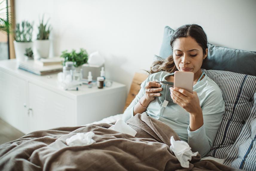 Sick person in bed checking phone for urgent care 