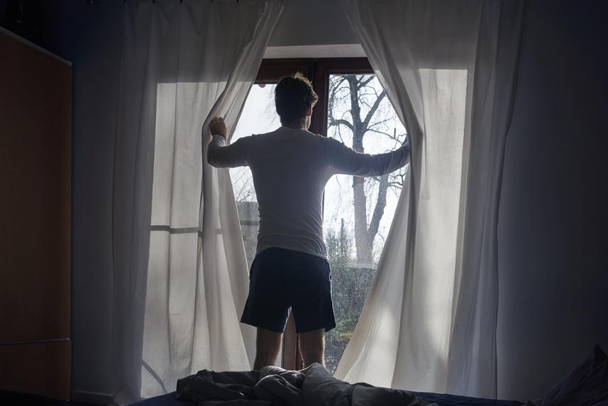 Man opening window curtains after daylight saving time 