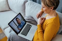 Woman sitting on a couch talking to a therapist via her laptop